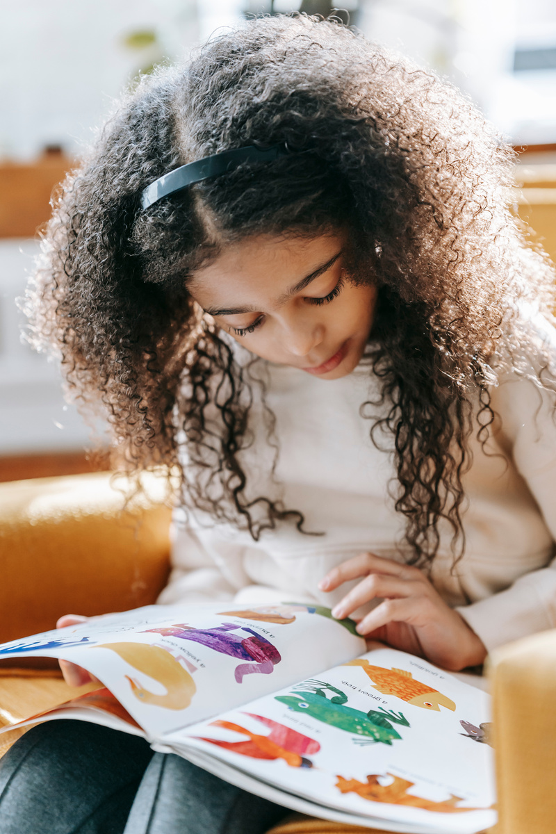 Focused black child studying colorful pictures in book at home